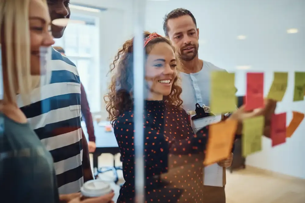 A small, diverse team working through coloured sticky notes on a glass wall together