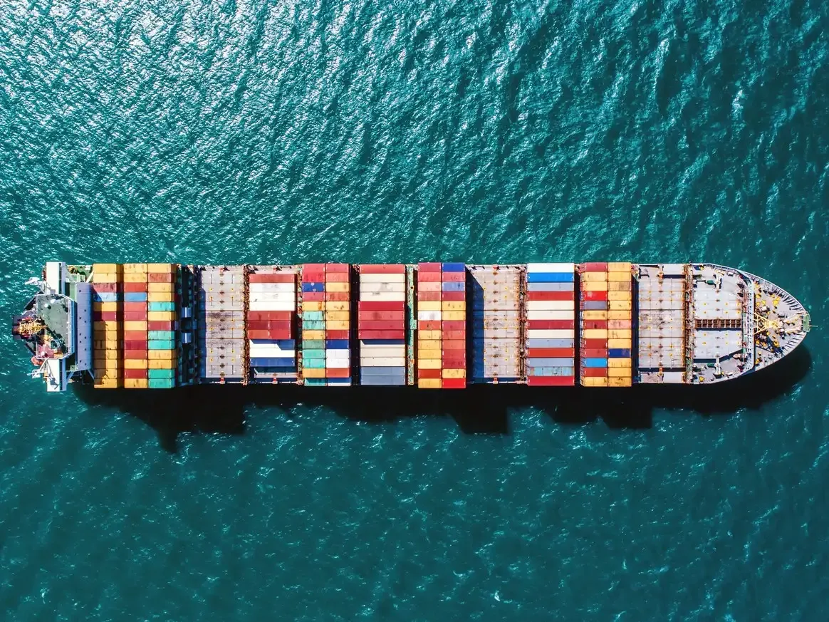 An aerial view of a container ship at sea, fully loaded with stacked shipping containers