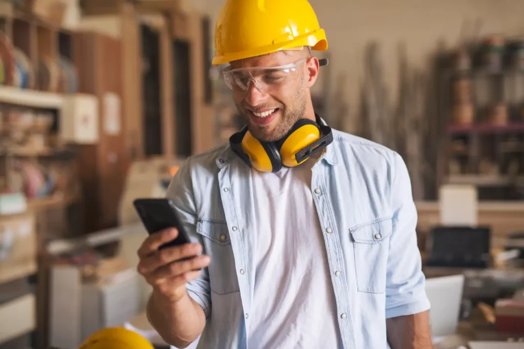 Een arbeider met zijn beschermende helm gebruikt graag zijn mobiele telefoon om te werken